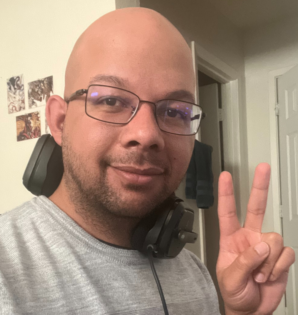 a selfie featuring brandon, with a pair of headphones around their beck, with their fingers offering the peace sign